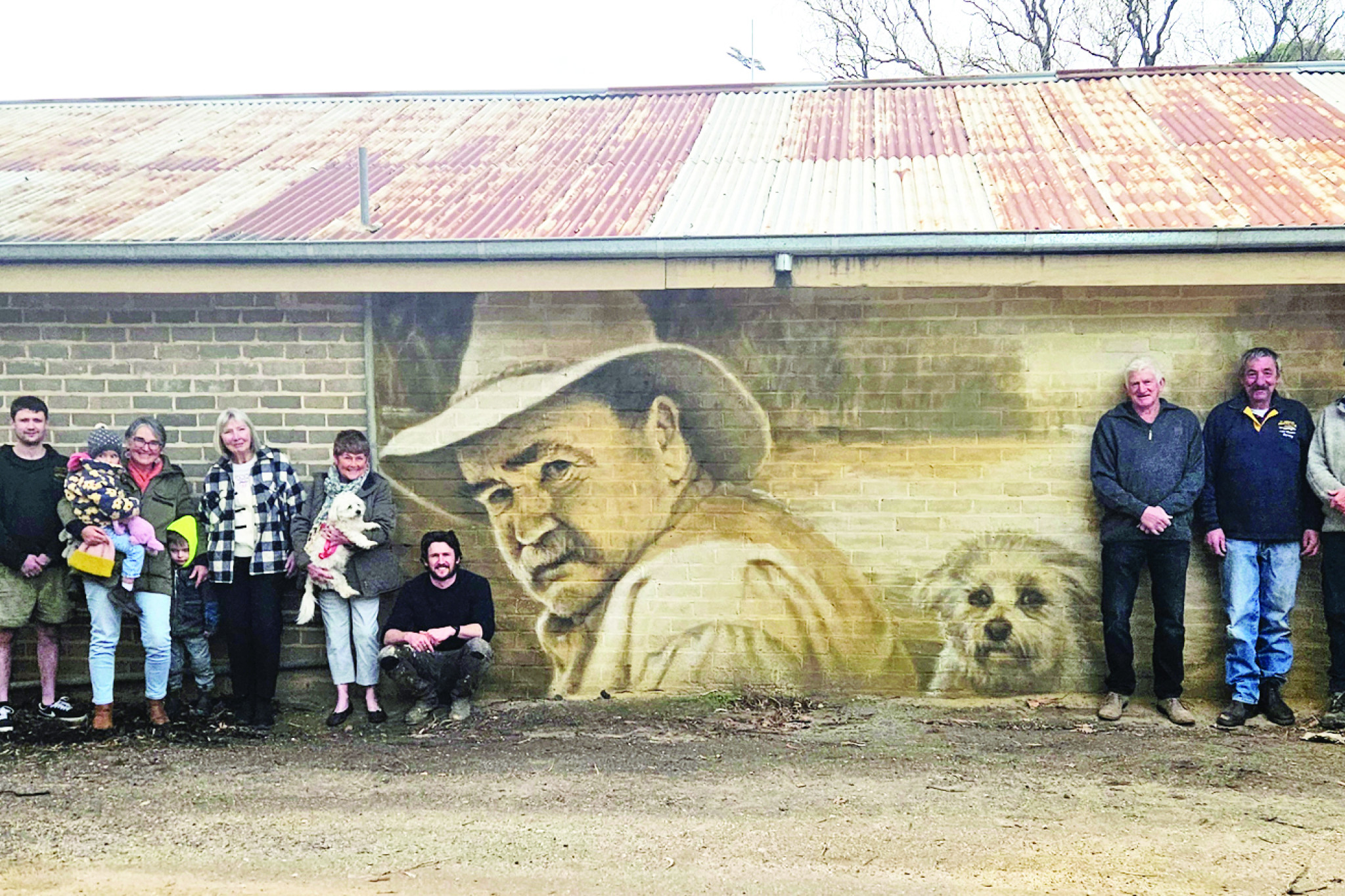 (left to right) Family: Robert Medlyn (brother), Austin Freeman (brother in law), Lyndon Medlyn (brother), Braydon Medlyn (grandson), Elma Coates (great niece) held by Deirdre Freeman (sister), Louis Coates (great nephew), Kay Medlyn (sister), Maree Medlyn (wife) holding dog Ernie who is featured in the painting, Kyle Torney alongside the painting of Neil Medlyn. Members of the St. Arnaud Angling Club were (left to right) Mervyn Evans, Wayne Ezard, Leo Burge, Michael Snow and Ivan Wild.